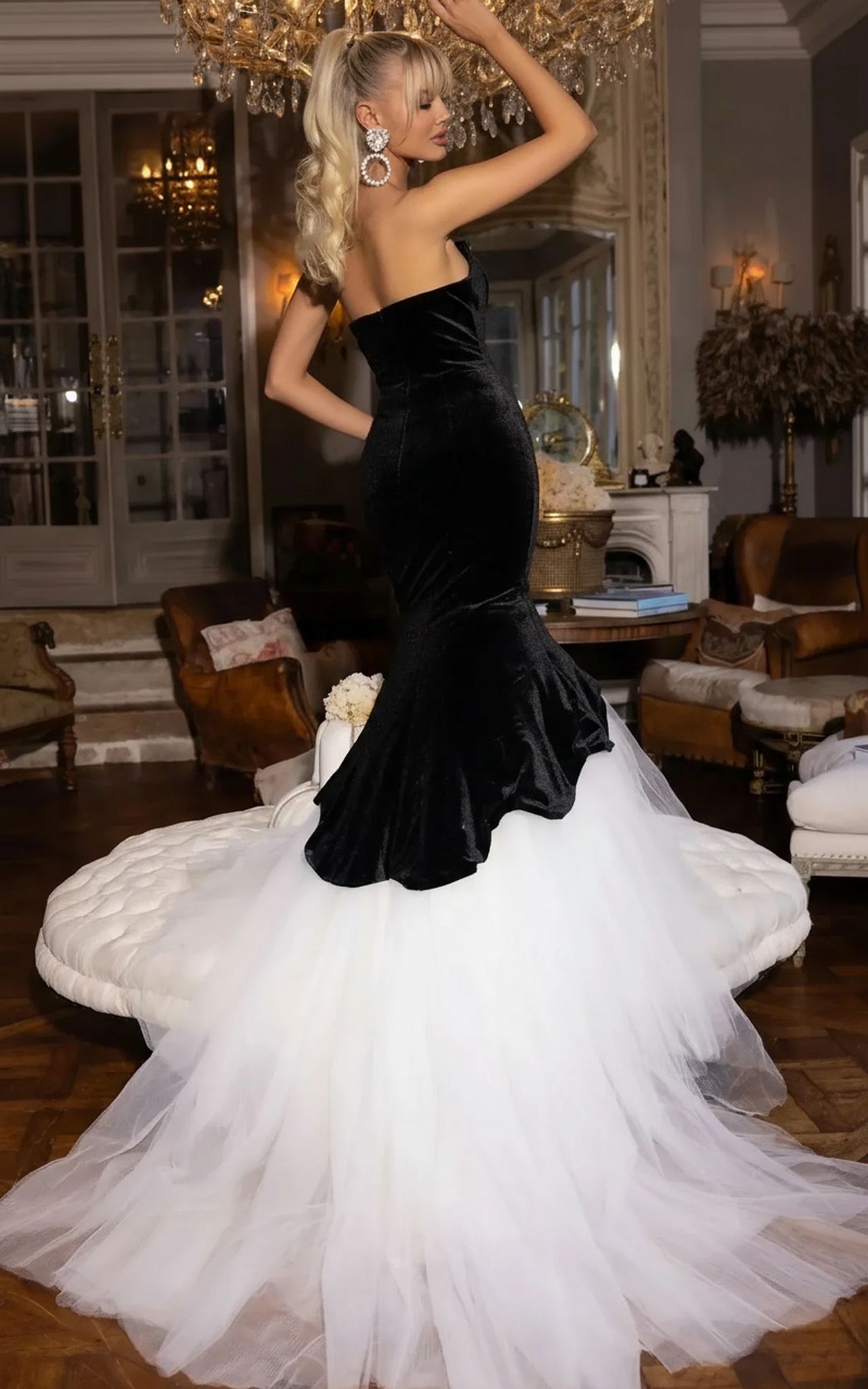 A woman poses indoors in the Portia and Scarlett PS25631E long prom dress—a strapless black velvet mermaid gown with a dramatic white tulle train—styled with earrings and a sleek ponytail.